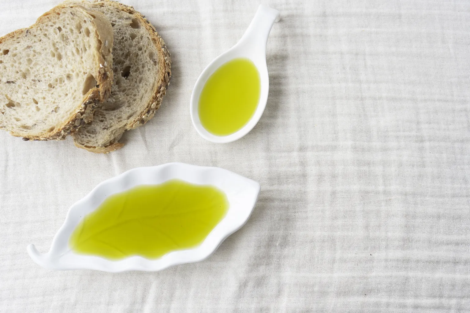 Beyaz örtü üzerinde ekmek dilimleri ve yaprak biçimli tabakta zeytinyağı